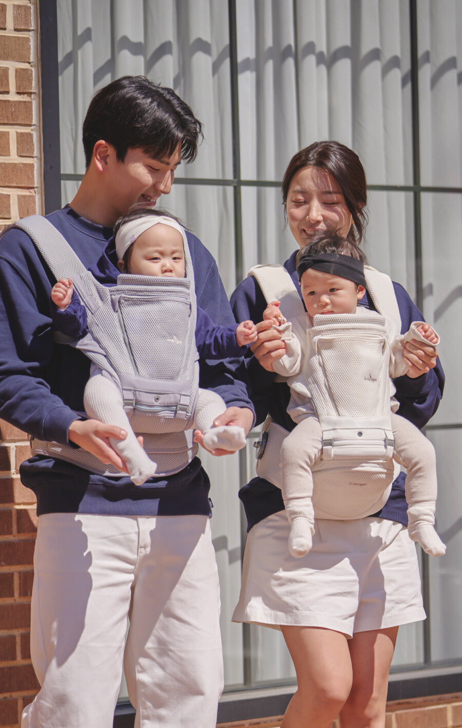 Two adults carrying babies in baby carriers outdoors.